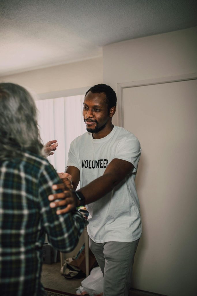 A compassionate volunteer helping a senior adult in a home setting.